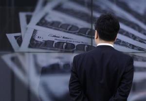A businessman looks at a screen displaying a photo of U.S. 100 dollar bank notes in Tokyo
